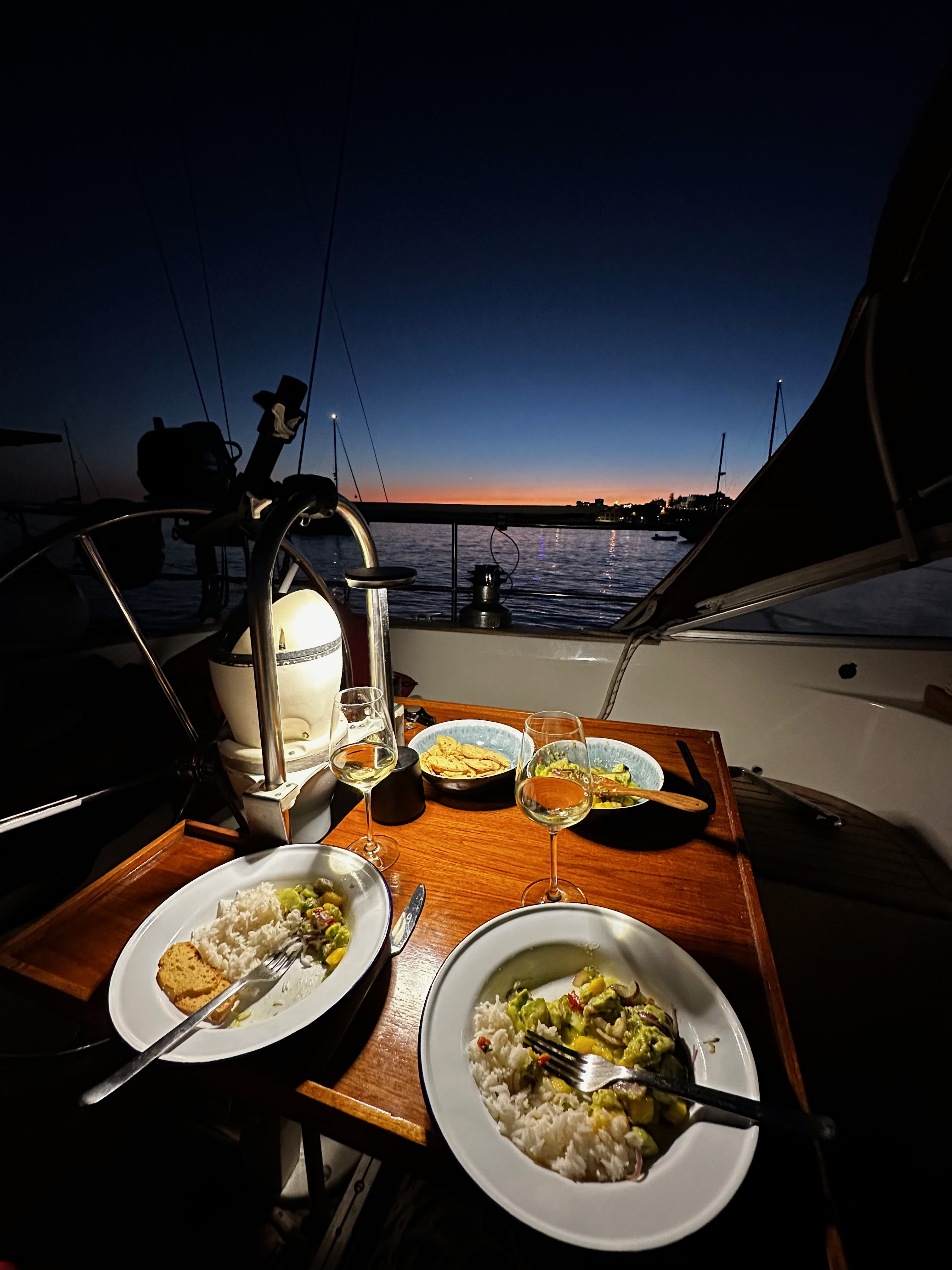 Dinner of curry and rice with wine glasses on a sailing yacht cockpit table at dusk