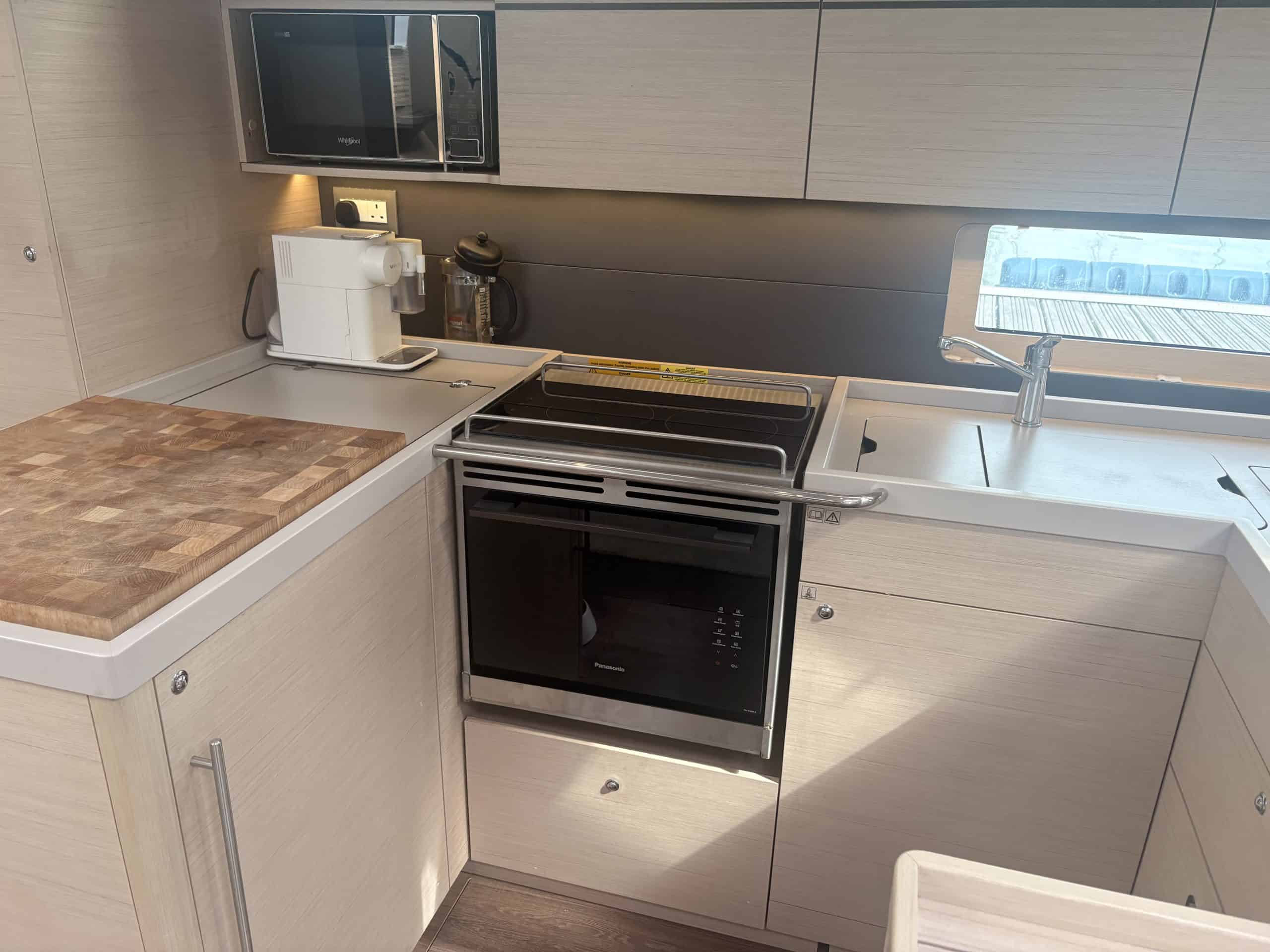 Curio electric galley enclosure fitted aboard a Beneteau Oceanis 51.1 — a Panasonic combination oven below a two-zone induction hob with a stainless fiddle rail, beside a butcher's-block worktop and the galley sink